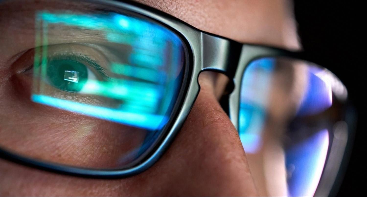 Close-up of a UAE IT engineer monitoring code and system alerts through blue-lit glasses